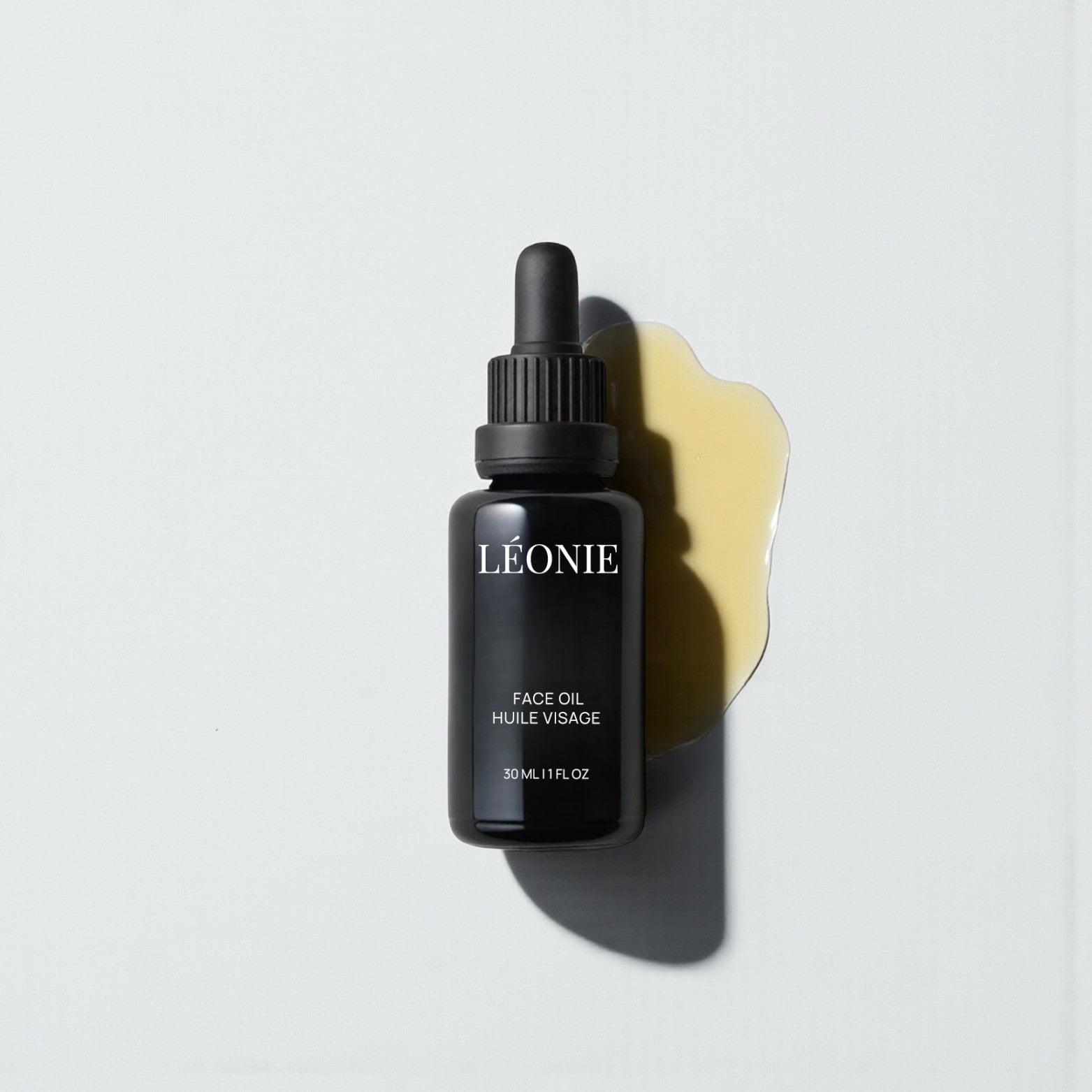 Black bottle of Léonie face oil with a dropper on a light gray background