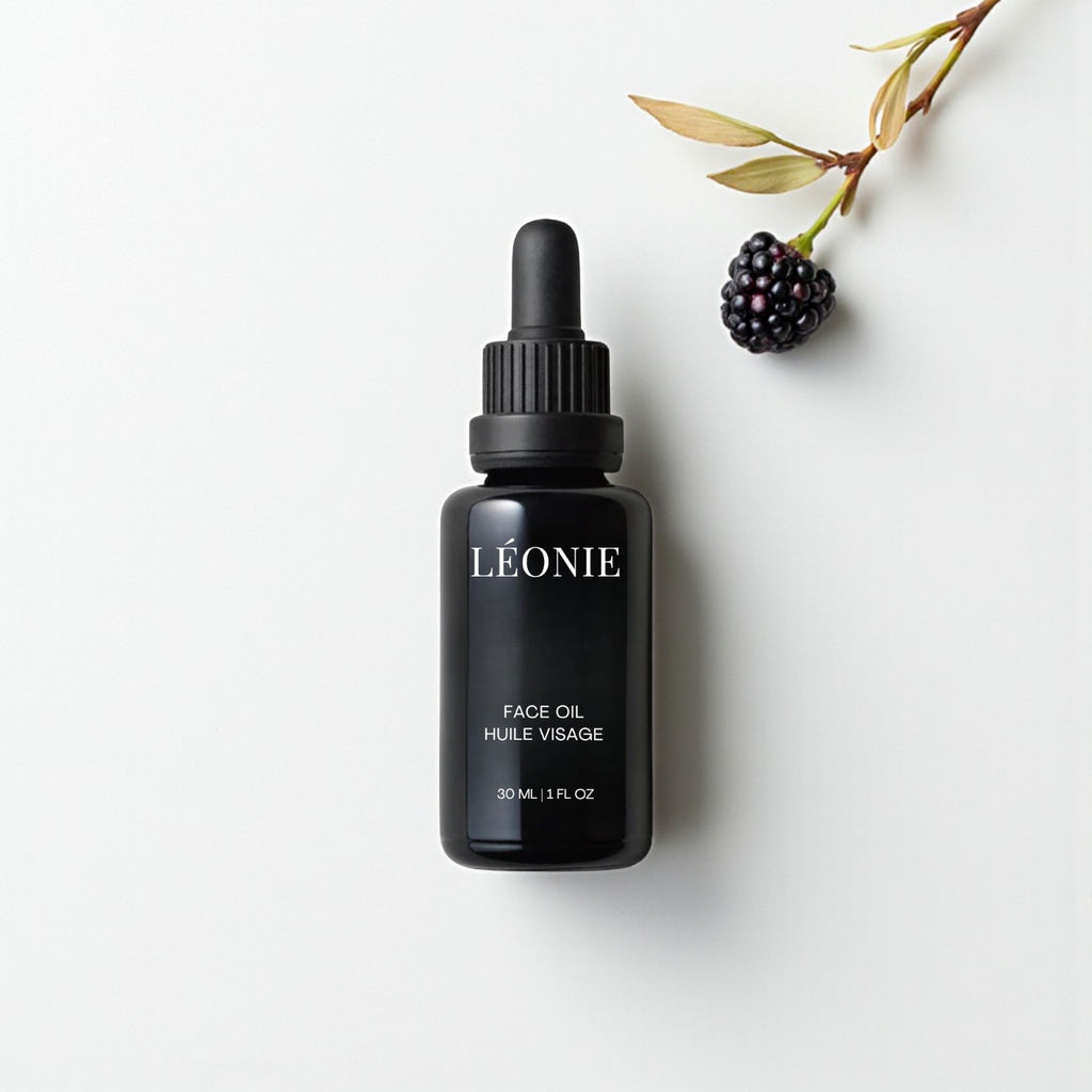 Black bottle of Léonie face oil on a white background with a black raspberry and leaves.